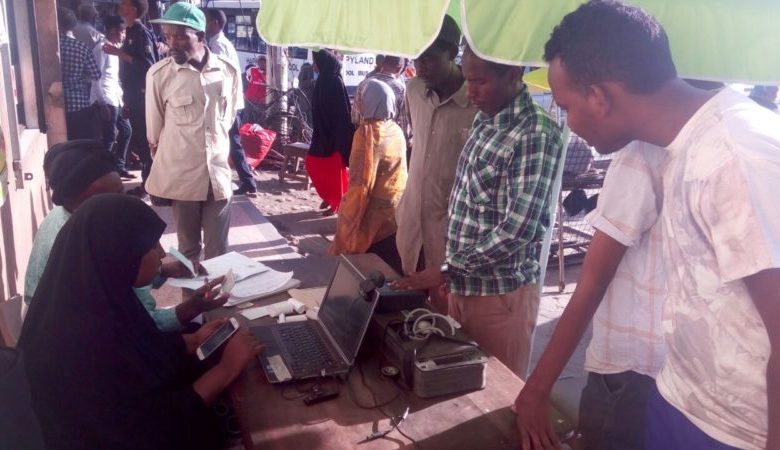 citizens look on curiously as one of them puts his fingers on the scanner for giving biomeric data at a voter registration place in Kenya during January / February 2017